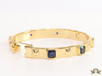 Band style bracelet in gold plating with gold plated details and sapphire blue colour stones