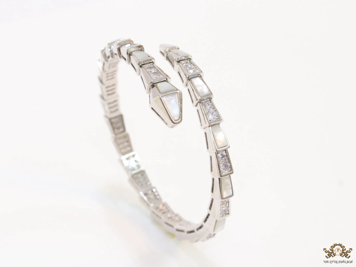 Open top platinum plated minimal serpentine bracelet with cubic zirconia stones and pearl white stones.