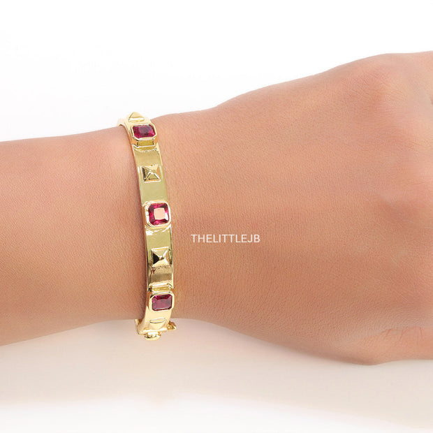 Band style bracelet in gold plating with gold plated details and ruby red colour stones