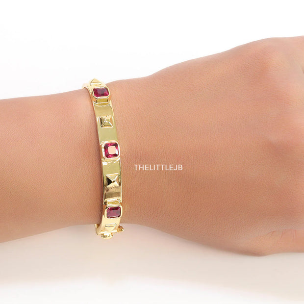 Band style bracelet in gold plating with gold plated details and ruby red colour stones