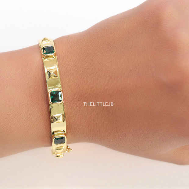 Band style bracelet in gold plating with gold plated details and emerald green colour stones