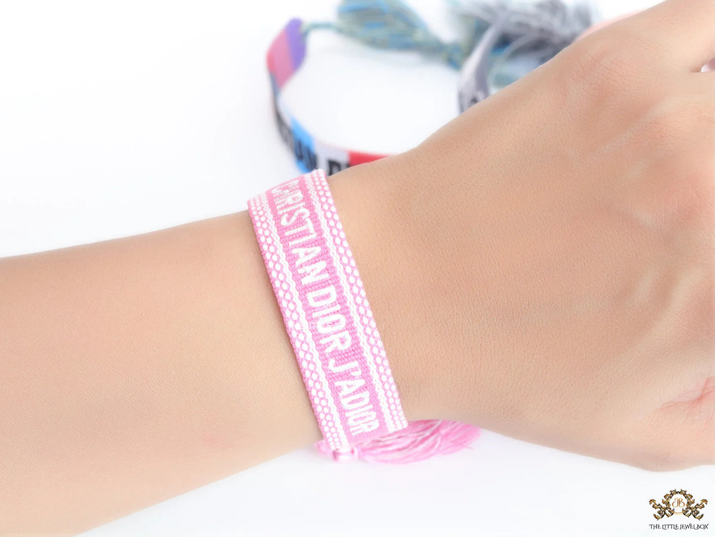 Adjustable pink woven bracelet with white knitted alphabets and tassels