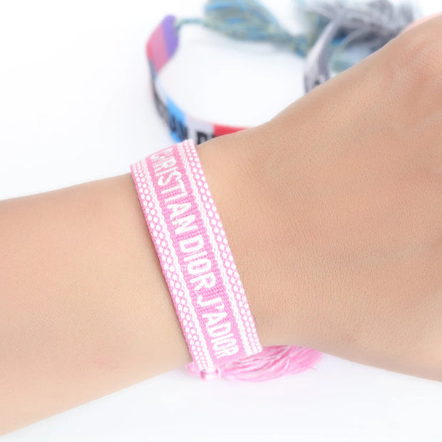 Adjustable pink woven bracelet with white knitted alphabets and tassels