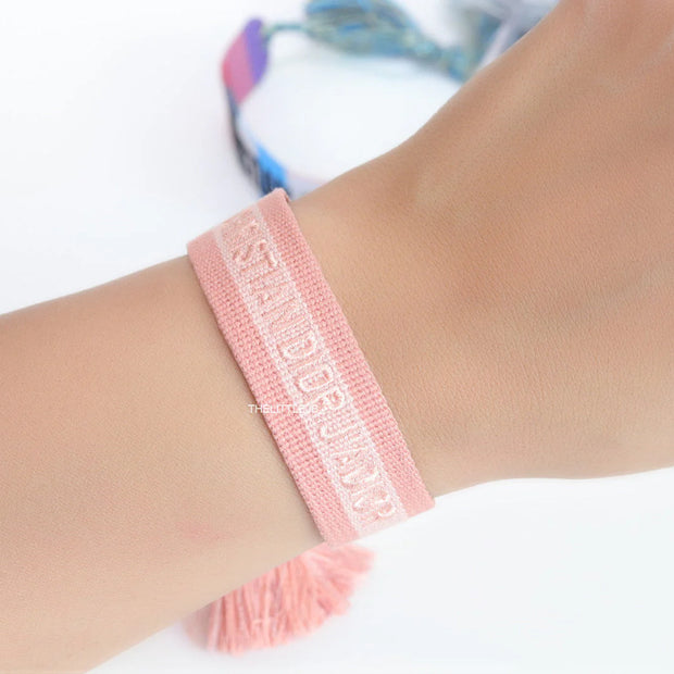 Adjustable pastel pink woven bracelet with knitted alphabets and tassels