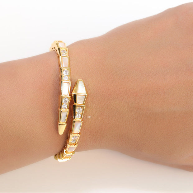 Open top gold plated minimal serpentine bracelet with cubic zirconia stones and pearl white stones.